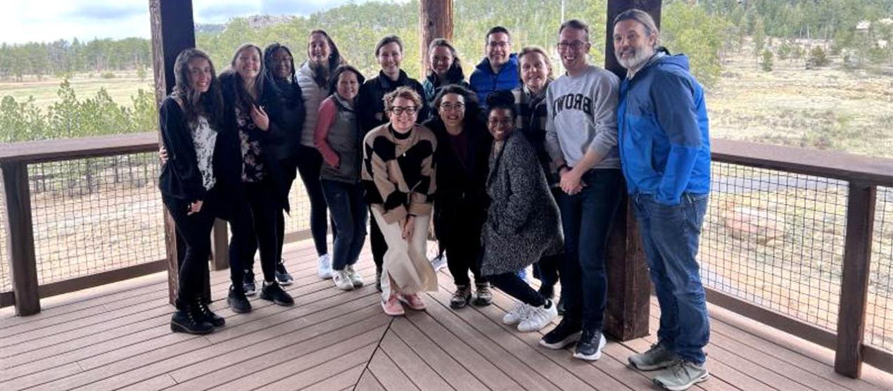 group of graduate students and professors posing on covered porch with forest in background